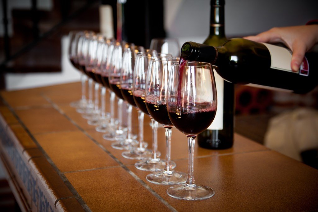 Woman hand with wine bottle pouring a row of glasses for tasting