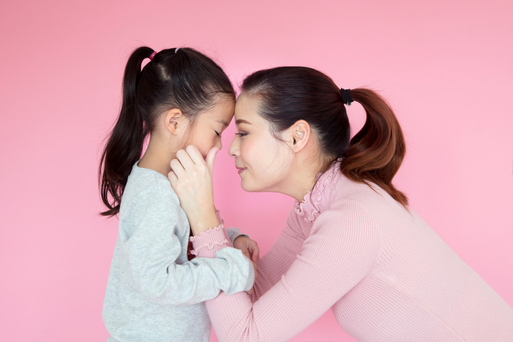 asian mother and child being affectionate against pink background