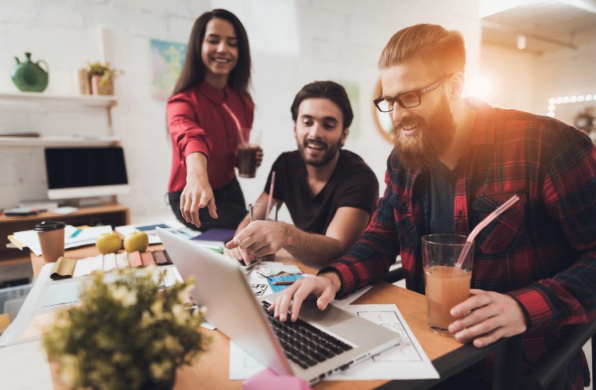 Three happy employees using a laptop inside an office